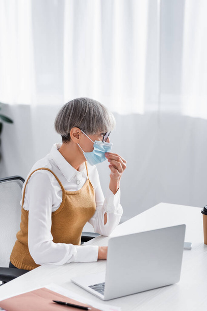 líder de equipe de meia-idade em óculos ajustando máscara médica no escritório - Foto, Imagem
