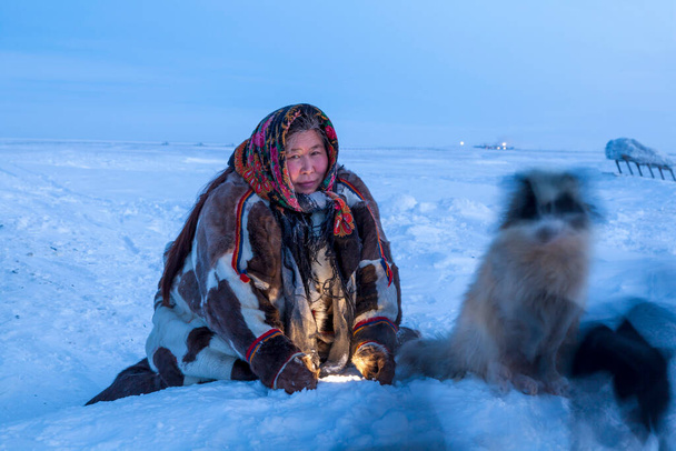 Una mujer, en la ropa de invierno nacional de los habitantes del norte de la tundra, juega con un perro en menos de 40, en la noche polar - Foto, imagen