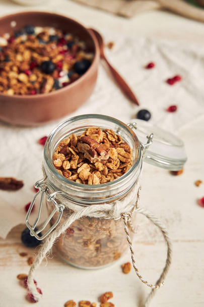 A vertical shot of delicious healthy vegan granola with pecan nuts in a fruity bowl with yogurt on a white table - Foto, Imagem