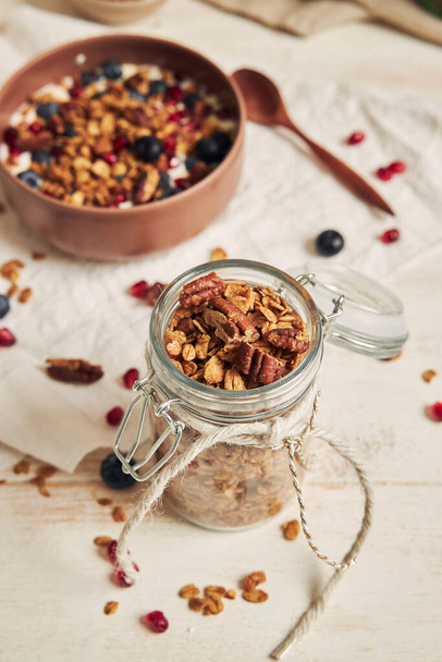 A vertical shot of delicious healthy vegan granola with pecan nuts in a fruity bowl with yogurt on a white table - Foto, Imagen
