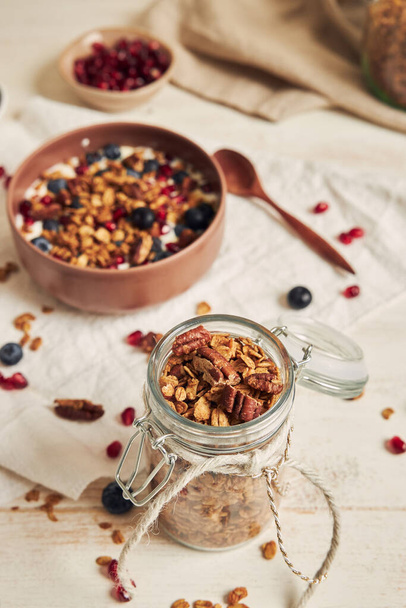 A vertical shot of delicious healthy vegan granola with pecan nuts in a fruity bowl with yogurt on a white table - Fotoğraf, Görsel