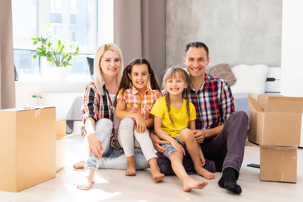 Vzrušená mladá rodina se baví v obývacím pokoji vybalování lepenkových krabic v den stěhování, šťastní rodiče hrát s dceruškami vyskočit z kartonu balíčku, přešťastný stěhování do nového domova spolu - Fotografie, Obrázek