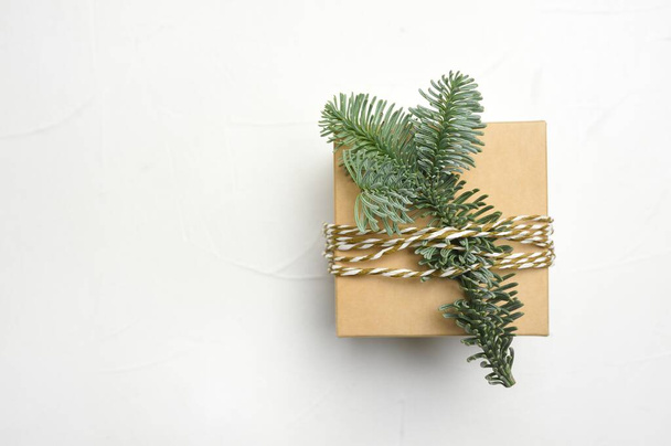 Christmas composition with green fir branches and kraft gift box on white wooden background with copyspace - Foto, Imagen
