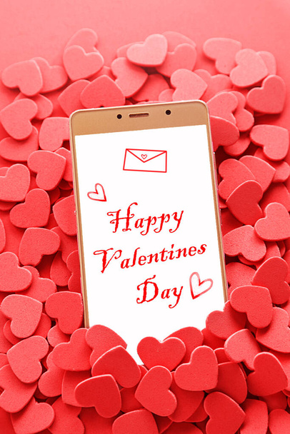 Hearts 'ın kırmızı arka planında cep telefonu var. Telefon ekranında Sevgililer Günün kutlu olsun. İnternetten randevulaşma. Sosyal medya randevu kavramı - Fotoğraf, Görsel