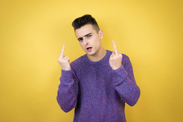 Young caucasian man over isolated yellow background showing middle finger doing fuck you bad expression, provocation and rude attitude. screaming excited - Fotó, kép