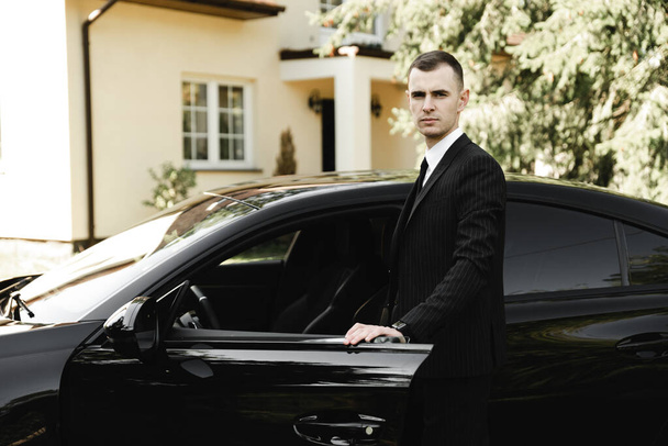 young successful businessman stands in front of his expensive car. rich young guy. rich man. car on the background of a businessman. groom with car on wedding day - Φωτογραφία, εικόνα