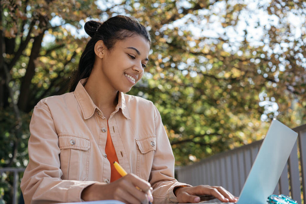 Afroamerykańska studentka korzystająca z laptopa, studiująca online, ucząca się języka, przygotowująca egzaminy. Bizneswoman pisze notatki, planuje proces pracy w miejscu pracy. Sprawy zakończone powodzeniem - Zdjęcie, obraz