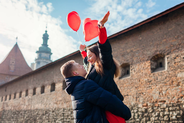 Valentines day couple in love. Man holding his girlfriend raising arms with balloons on city street. People having fun outdoors. - Photo, Image