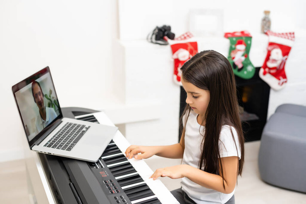 Mała dziewczynka ma lekcję online z nauczycielem gry na pianinie w czasie Bożego Narodzenia - Zdjęcie, obraz