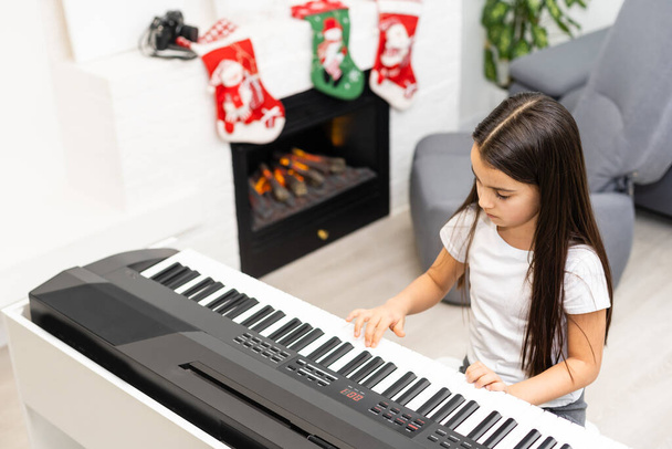 Linda niña toca la melodía de Navidad en el piano, feliz celebración de Navidad, felices fiestas de temporada - Foto, imagen