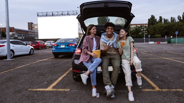Jonge vrolijke multiraciale vrienden in de auto op bij auto cinema - Foto, afbeelding