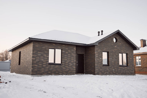 One-story brick house on the background of a snowy winter evening. Construction of low-rise buildings for further sale. Concept of building business. - Fotografie, Obrázek