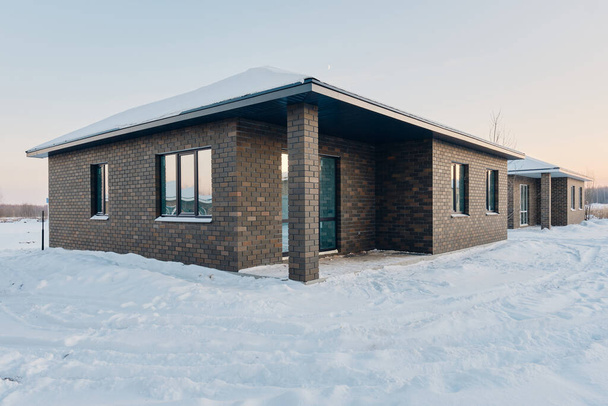 One-story brick house on the background of a snowy winter evening. Construction of low-rise buildings for further sale. Concept of building business. - Fotó, kép