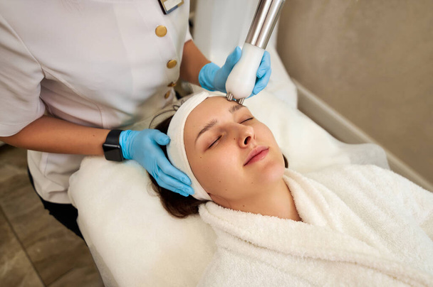 Красивая женщина получает лечение микротоком лица от косметолога в салоне красоты - Фото, изображение