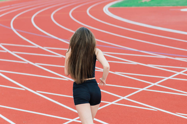 Jong, mooi meisje atleet in sportkleding is training en hardlopen, stretching in het stadion - Foto, afbeelding
