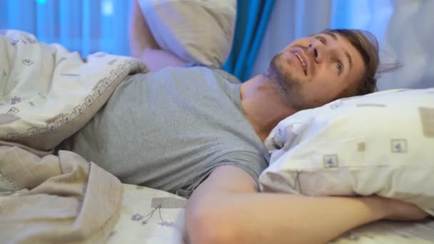 Egy fiatal, dühös férfi próbál aludni, miközben párnával takarja a fülét. Zajos szomszédok - Felvétel, videó