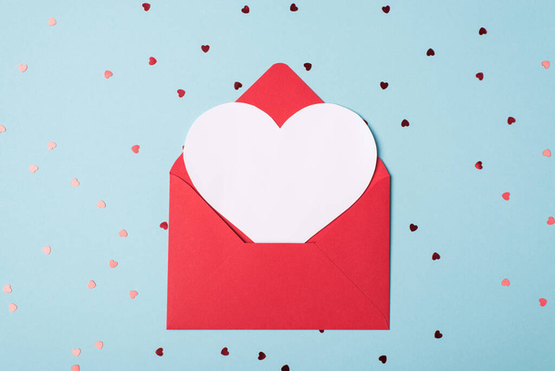 Сверху над квартирой лежит фотография открытого конверта с валентинкой внутри для макета на пастельном фоне с блестящими блестками - Фото, изображение