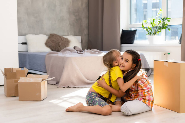 Happy family in living room. Preschool daughters sitting and help unpacking cardboard boxes belongings. Buy real estate, relocation at new modern house - Photo, Image