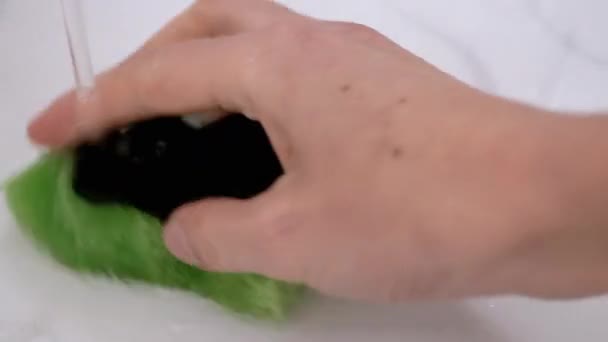 Samičí ruka stiskne zelenou houbu s pěnou pod tekoucí vodou v umyvadle - Záběry, video
