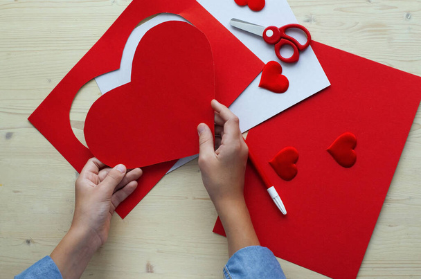  DIY ünnepi kártya piros papírszívvel, a szerelem szimbóluma. Anyák napja, Valentin-nap, szülinapi üdvözlőlap. Hobbi, gyermekművészet koncepció, ajándék saját kezűleg, DIY ötletek gyerekeknek - Fotó, kép