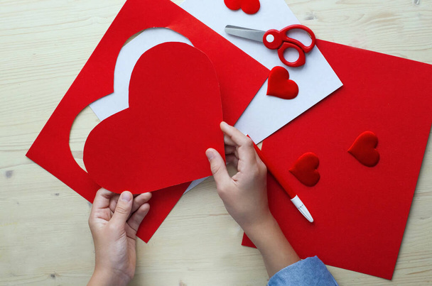  DIY lomakortti punaisella paperilla sydän, rakkauden symboli. Poika tekee äitienpäivän, ystävänpäivän, syntymäpäiväkortin. Harrastus, lasten taidekonsepti, lahja omin käsin, DIY Ideat lapsille - Valokuva, kuva