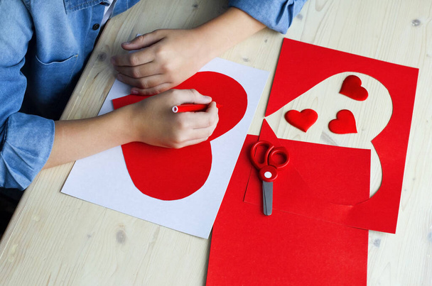  赤い紙の心、愛のシンボルとDIY休日カード。子供は母の日、バレンタインデー、誕生日の挨拶カードを作ります。趣味、子供のアートコンセプト、あなた自身の手で贈り物、子供のためのDIYアイデア - 写真・画像