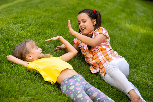 家の裏庭で戦っている2人の女の子の姉妹の肖像画。友達の女の子が楽しんでいる。一緒に遊んでいる兄弟のライフスタイル率直な家族の瞬間. - 写真・画像