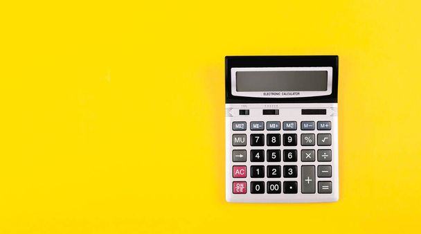 Large silver calculator with black buttons on yellow background with copy space. Conceptual photo of calculations, counting, accounting, computing, profit, loss, tax. Business card. Digital stationery - Foto, Imagen