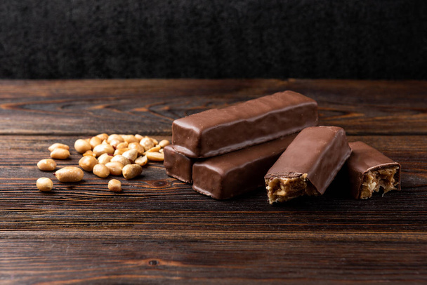 Шоколадний бар з карамеллю та арахісом на темному дерев'яному фоні
. - Фото, зображення