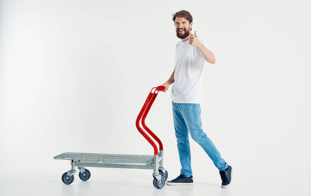 cargo trolley man in jeans and sneakers light background work transportation - Foto, Imagen