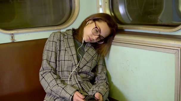 Młoda kobieta zasnęła w metrze. Dziewczyna ze słuchawkami w uszach. Stary wagon metra - Zdjęcie, obraz