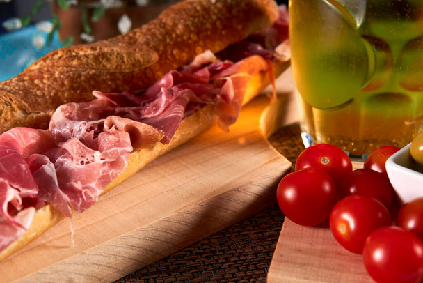 Сэндвич из вяленой ветчины также известен как Bocadillo de jamon serrano с гарниром из помидоров и оливок и вкусным пивом. - Фото, изображение