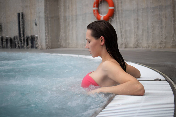Mujer seductora en sujetador rosa cruzando brazos y mirando hacia otro lado mientras descansa en agua limpia de aguas termales en el resort - Foto, imagen
