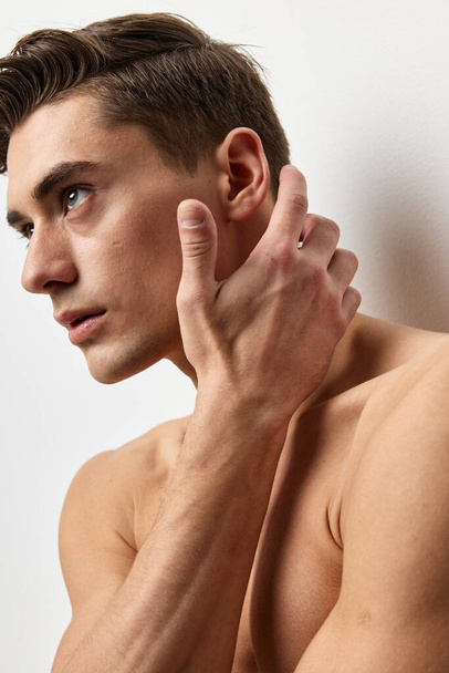 A sexy guy with a naked torso touches his face with his hand and looks to the side - Photo, Image