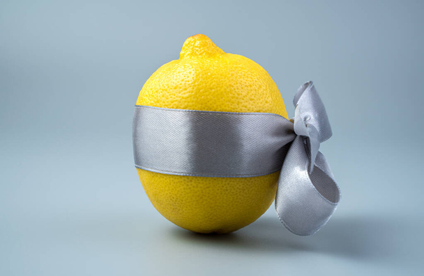 Een gele citroen is gebonden met een grijs lint op een grijze achtergrond. - Foto, afbeelding