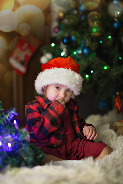 a child in red clothes is sitting waiting for the new year. the concept of celebrating Christmas at midnight. holiday costume - Foto, immagini
