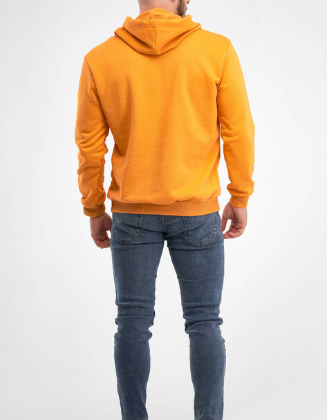 Człowiek stojący w pomarańczowej bluzie. Samiec w odosobnionym studio, ubrany na makiecie. wzór wzoru kaptura - Zdjęcie, obraz