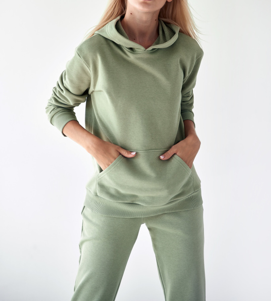 Açık yeşil kapüşonlu ve pantolonlu bir kız. Spor kıyafetleri satışı için stüdyo çekimi - Fotoğraf, Görsel