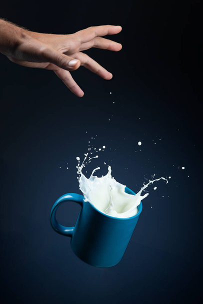 Copo de leite com respingo caindo da mão sobre fundo azul escuro . - Foto, Imagem