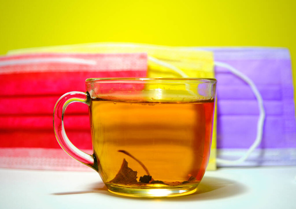 Φυτικό και linden τσάι σε γυάλινο δοχείο και linden αφήσει μέσα στην κατσαρόλα με πολύχρωμο κόκκινο και κίτρινο φόντο ιατρική μάσκα. - Φωτογραφία, εικόνα