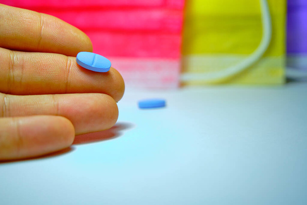 Pilules bleues sur la main et fond de masques médicaux colorés. - Photo, image