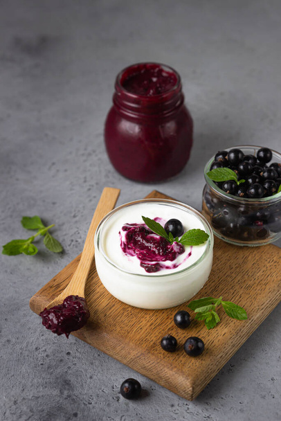 Jar of delicious homemade black currant curd, custard or jam with natural yogurt and fresh berries on grey background. Healthy breakfast. - Zdjęcie, obraz