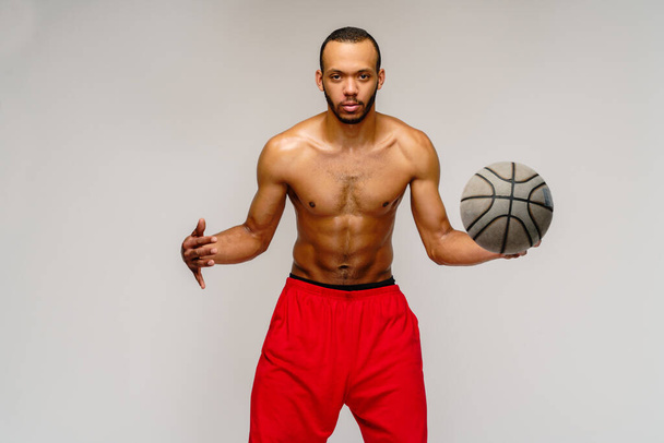 Muscular african american sportsman playing basketball shitless over light grey background - Foto, Imagen