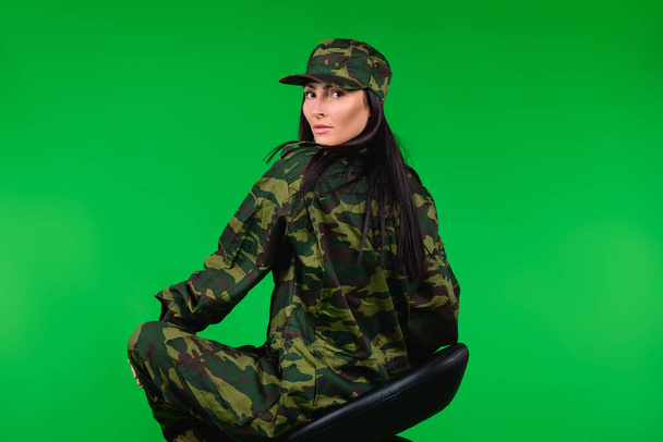 A photo from the back of a woman in a military uniform on a black chair and a green background. High quality photo - Foto, immagini