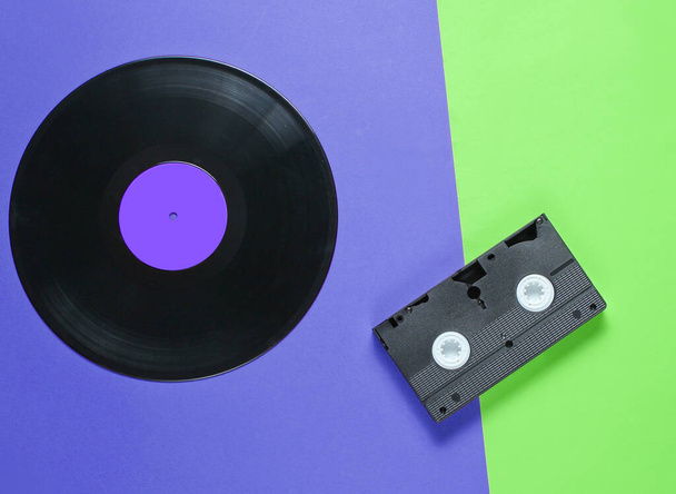 Verouderde videocassette, retro audiocassette, vinyl plaat op een papieren achtergrond van twee ton, popcultuur. Bovenaanzicht. Minimalisme - Foto, afbeelding