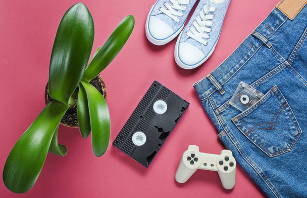 saia jeans estilo retro feminino casual, cassete de vídeo, gamepad, tênis sapatos, panela com uma planta verde no fundo vermelho. Cultura pop, minimalismo - Foto, Imagem