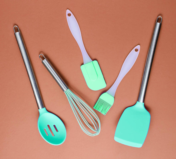 Herramientas de silicona con asas metálicas para cocinar sobre fondo marrón - Foto, imagen