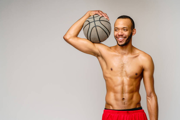 Muscular african american sportsman playing basketball shitless over light grey background - Foto, immagini