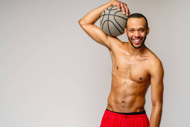 Muscular african american sportsman playing basketball shitless over light grey background - Photo, image
