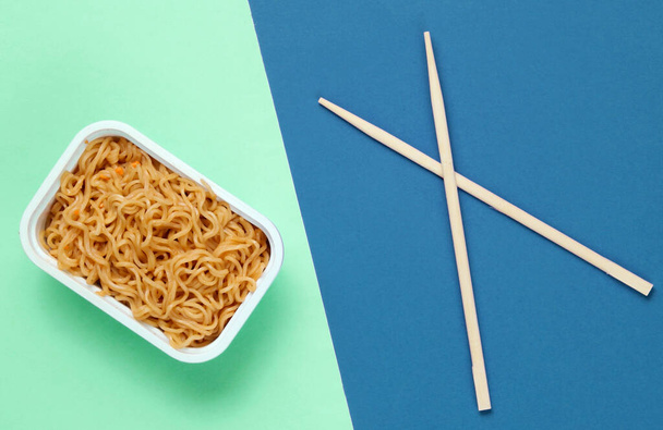 Instant noodles and chinese chopsticks on blue green background, minimalism. Top view - Photo, Image